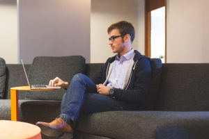 young man with glasses sitting on a couch using a laptop