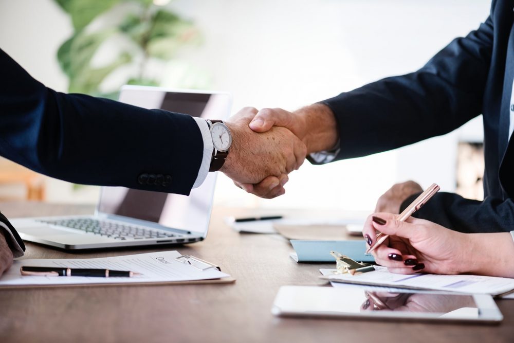 Two men shaking hands and a woman's hand writing down on a document