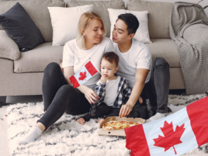 woman and husband with their child holding a Canadian flag, pizza on the ground, and another Canadian flag on the bottom right