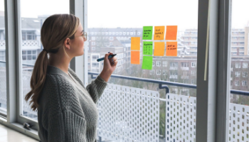 blond female worker standing in front of a window and writing on sticky notes