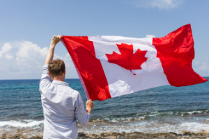 man holding up Canadian flag at the beach